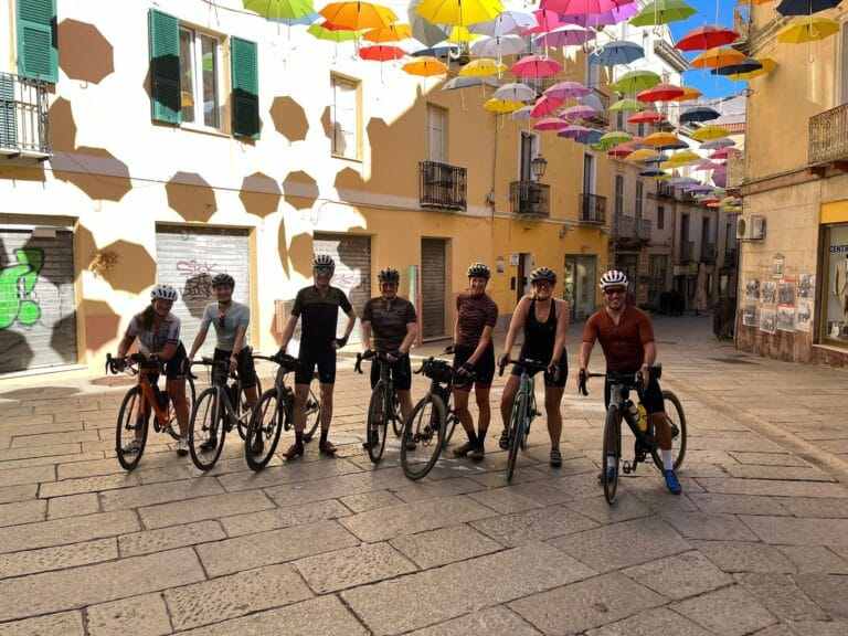 fietsers-rudirides-sardinie-stad-iglesias-gekleurde-paraplus Groep van Rudi Rides in centrum Iglesias, Sardinie met paraplu versiering