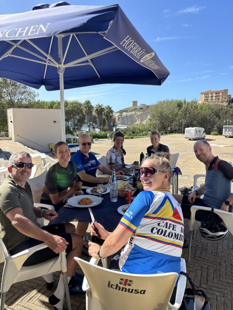 rudi-rides-lunch-in-zon-op-sardinie-westkust-torri Groep fietsers in de zon op het terras op Sardinie westkust