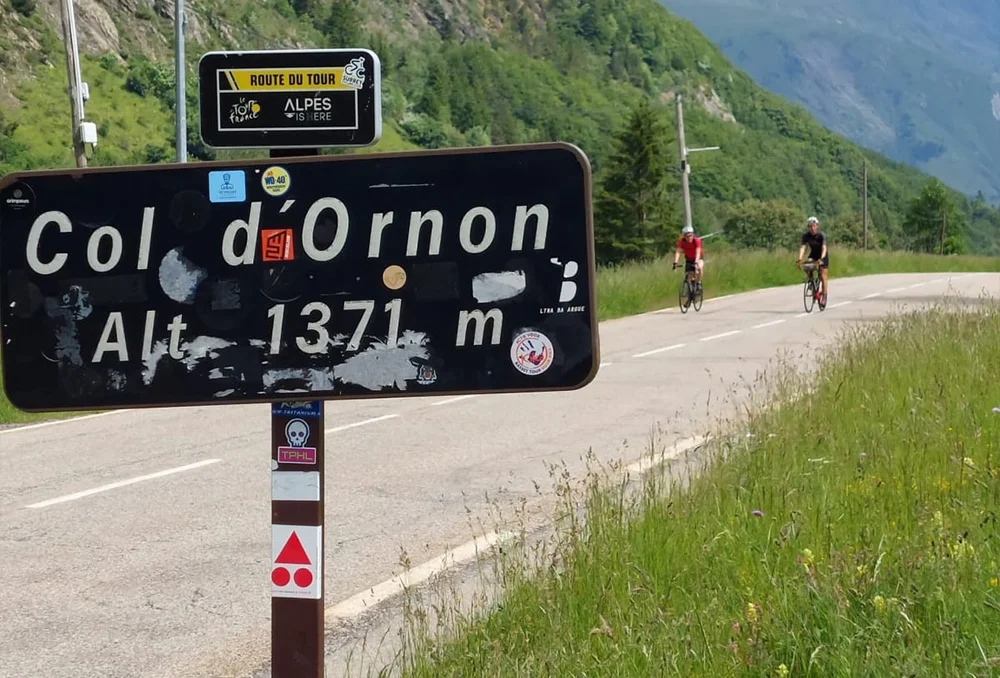 Col d'Ornon colbord met op achtergrond twee wielrenners.