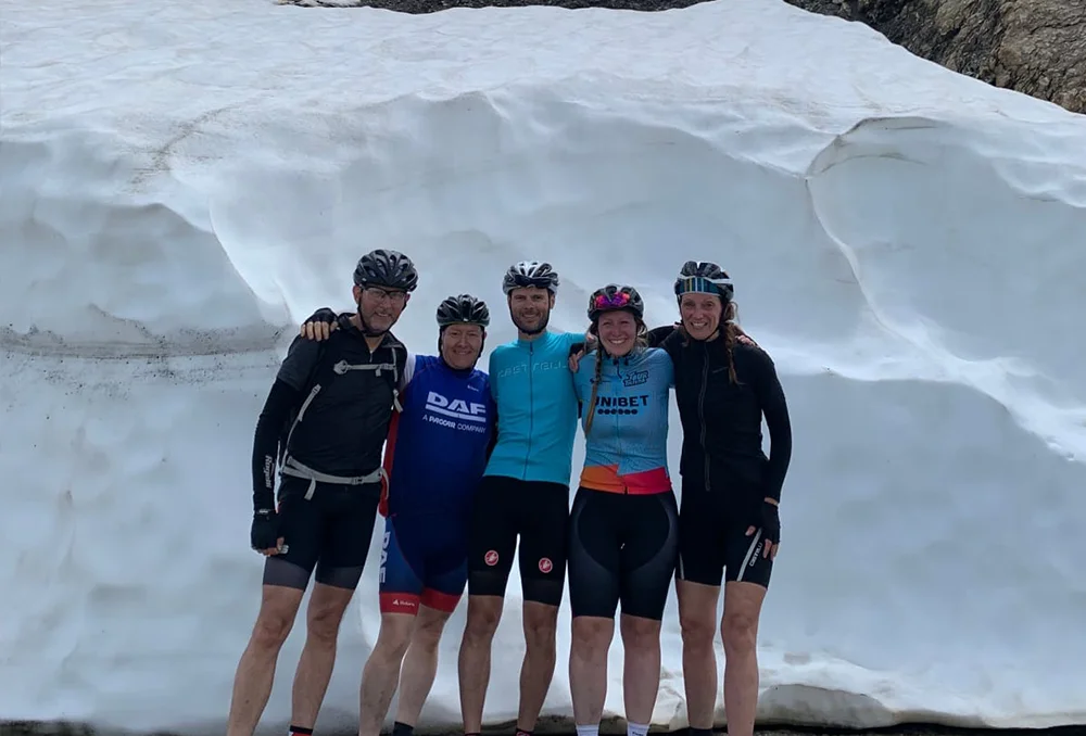 Groep wielrenners op Col du Galibier met op achtergrond veel sneeuw. In juni.