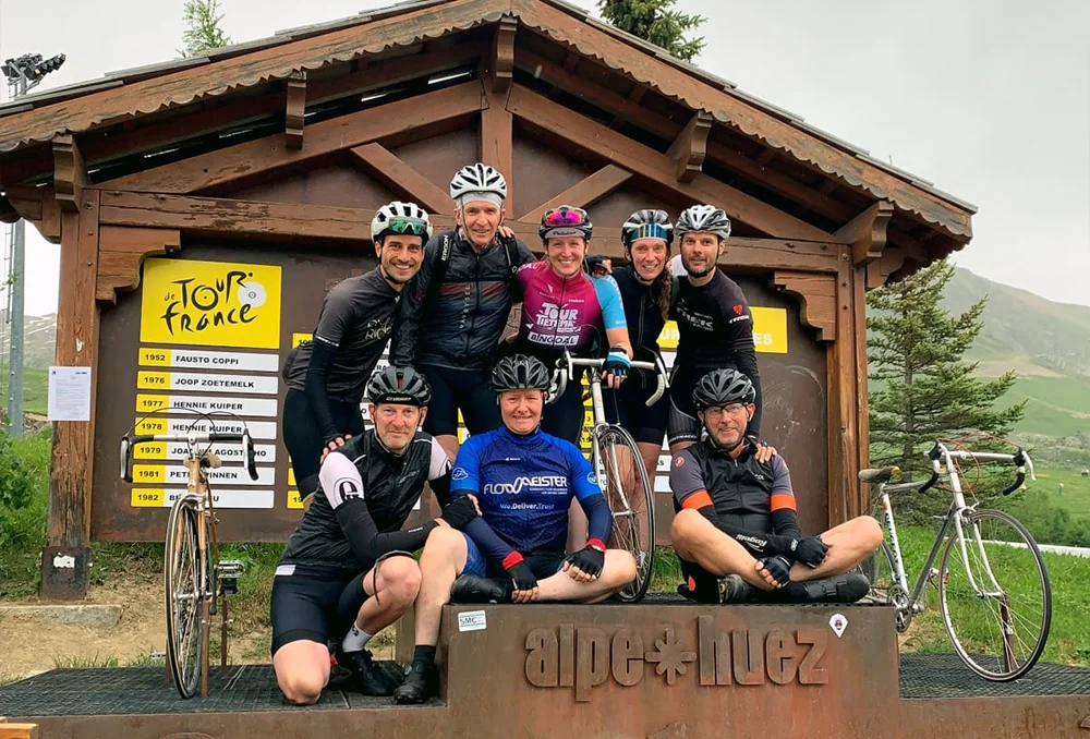 Groepsfoto Rudi Rides bovenop de Alpe d'Huez bij het bekende huisje met Tour de France bord