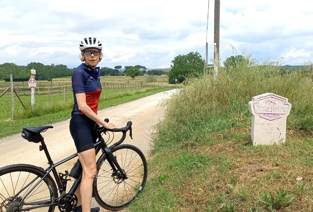Vrouwelijke fietser bij een bordje van Strade Bianche in Toscane Italië