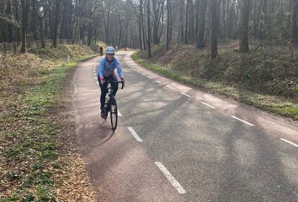 Vrouwelijke wielrenner op asfaltweg door een bos met kale bomen in het Nederlandse voorjaar