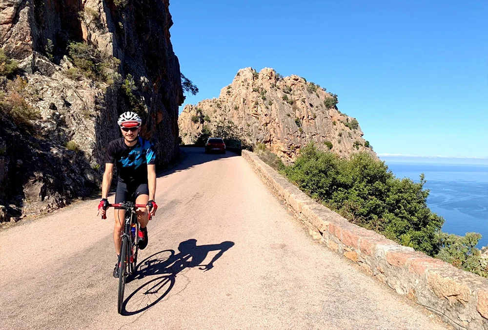 Fietser met Sunweb pet aan de kust van Corsica dichtbij UNESCO erfgoed Calanches de Piana